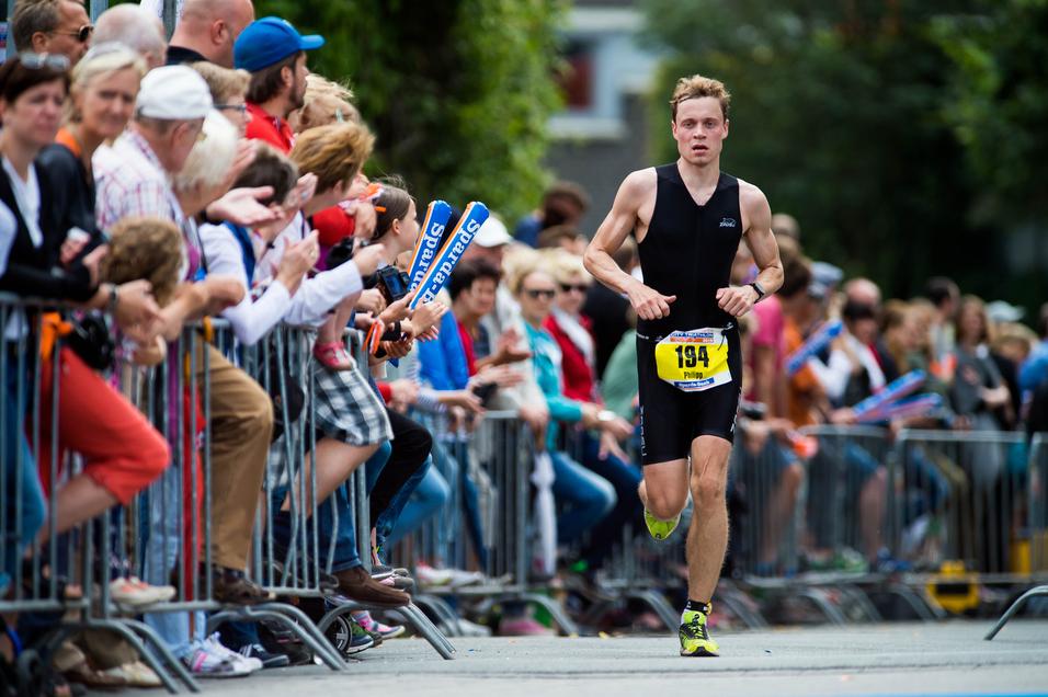 Ein Athlet sprintet entlang einer Zuschauerreihe bei einem Wettkampf, während die Menge jubelt und applaudiert.
